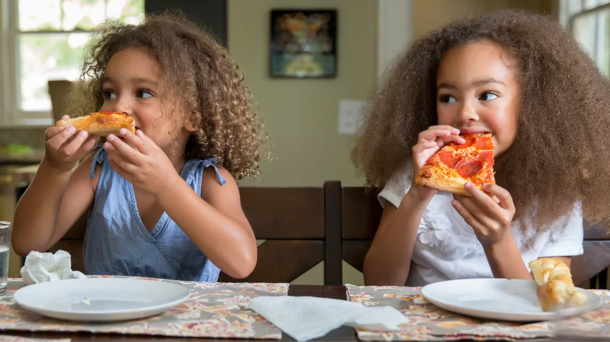 Two little girls eating pizza.