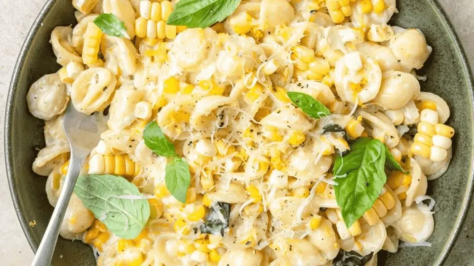 Plate of creamy pasta with sweet corn and basil, drizzled with olive oil, offering a vibrant and appetizing presentation.