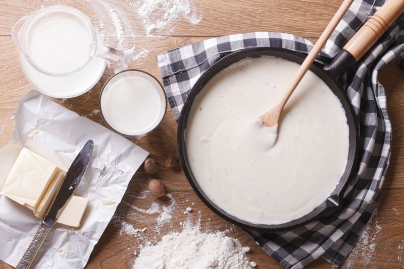 Mesa con harina e ingredientes lácteos y una sartén con una mezcla para panqueques