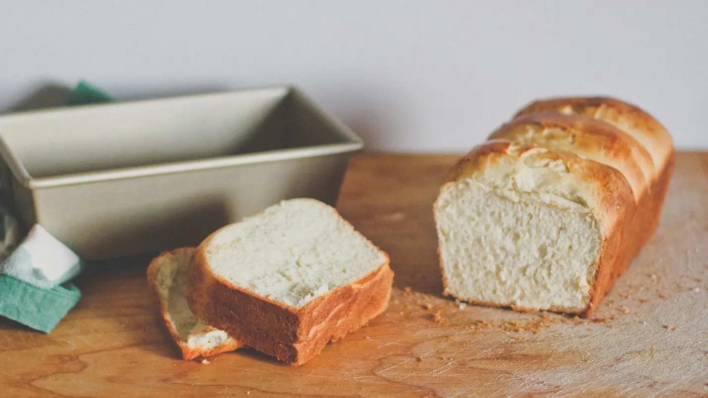 Loaf of freshly baked classic white bread with a golden crust, sliced to reveal its soft and fluffy interior, ideal for sandwiches and toasting.
