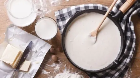 Table with flour and dairy ingredients and a pan with a pancake mixture
