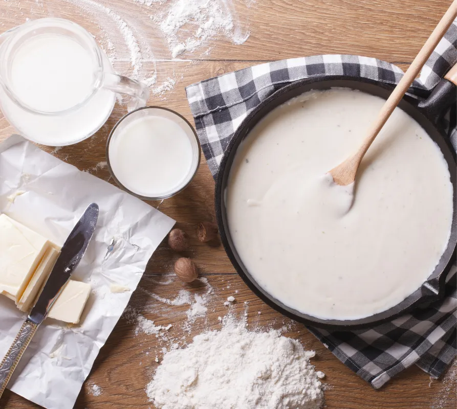 Table with flour and dairy ingredients and a pan with a pancake mixture