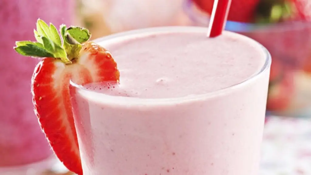 Creamy banana strawberry licuado served in a tall glass, garnished with fresh banana slices and strawberries, offering a refreshing and nutritious beverage.