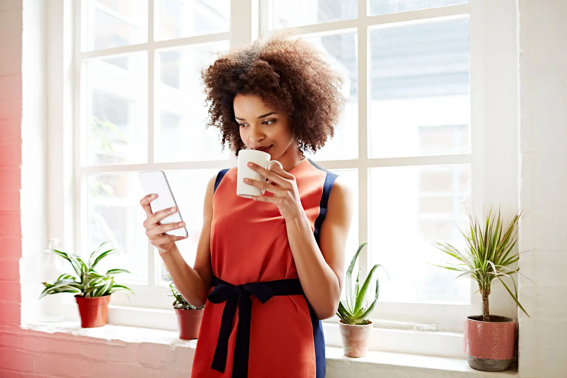 A black young woman drinking in a cup and holding a cellphone in her hand