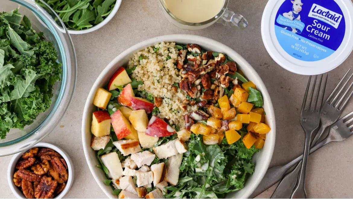 Colorful salad with quinoa, chicken, apples, and kale, topped with Lactaid® Sour Cream, alongside apples and nuts