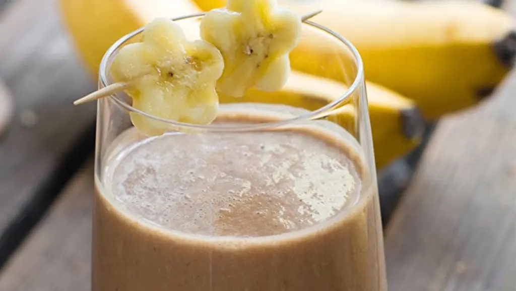 Creamy chocolate banana shake served in a tall glass, topped with whipped cream and chocolate shavings, garnished with a banana slice for a delicious treat.