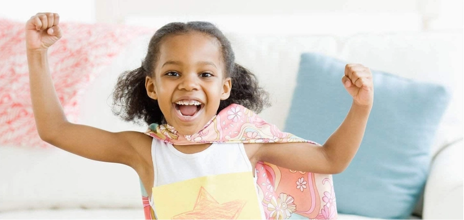 A smiling little girl wearing a superhero cape.