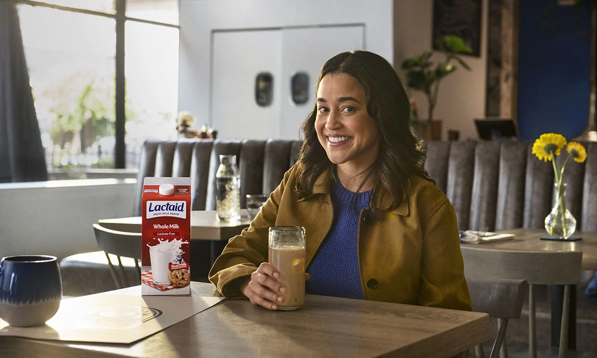 Customer sitting in a cozy café holding a glass of iced latte, with a carton of Lactaid Whole Milk on the table.