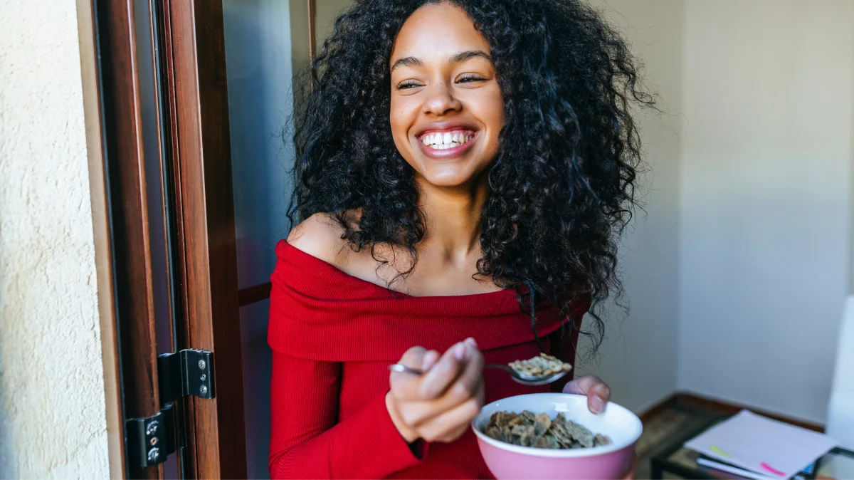 Woman smiling as she eats a bowl of cereal.