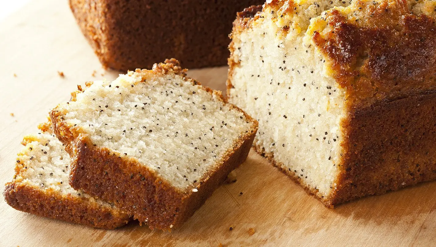 Sliced poppy seed tea bread on a wooden cutting board, showcasing its moist texture and sprinkled with poppy seeds, ideal for afternoon tea or breakfast.
