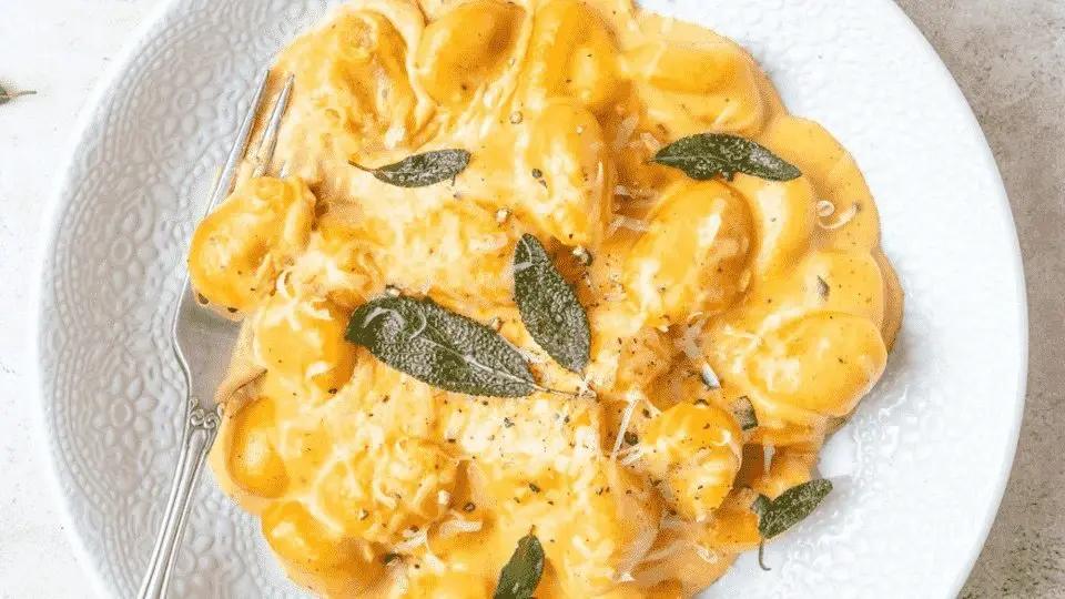 Plate of creamy pumpkin gnocchi drizzled with sauce, garnished with sage leaves, offering a comforting autumn-inspired meal.