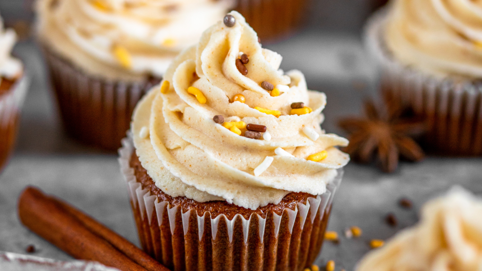 Moist pumpkin spice cupcakes topped with creamy maple buttercream frosting, garnished with a sprinkle of cinnamon, served on a decorative plate for a festive treat.
