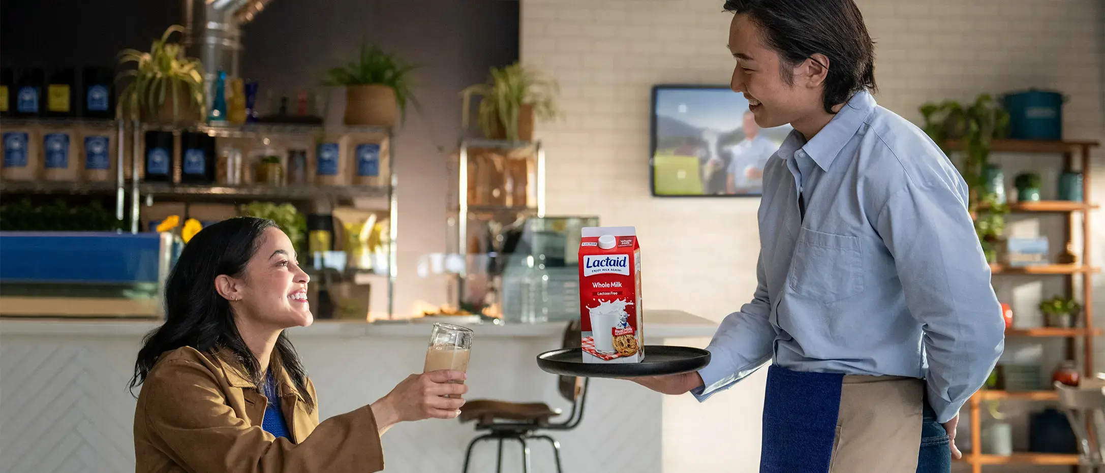 Server presenting a carton of Lactaid Whole Milk on a tray to a customer holding a glass of iced beverage in a cozy café setting.