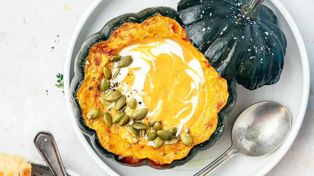 Acorn squash soup topped with cream and pumpkin seeds with spoon