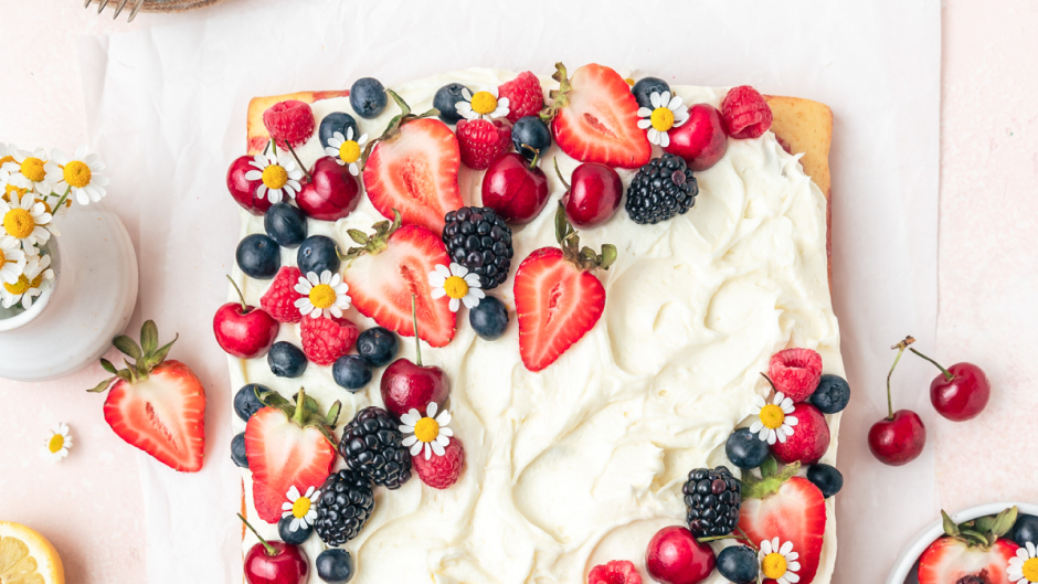 Delicious roasted berry sheet cake topped with fresh berries and a dusting of powdered sugar, served on a wooden cutting board.
