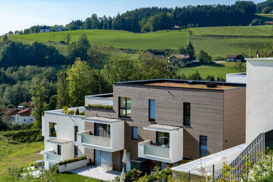 Haus mit Flachdach sowie Balkonen und Dachterrasse in flacher Lage und grüner Umgebung 