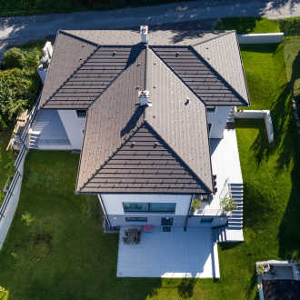 Einfamilienhaus mit Steildach wird von oben abgelichtet und zeigt die schön verlegten Dachsteine von BMI Bramac sowie eine kleine Terrasse mit schönem Garten zum Entspannen