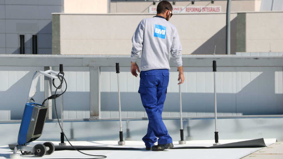 BMI Österreich Mitarbeiter verlegt Everguard von BMI Bramac auf Flachdach bei schönem Wetter