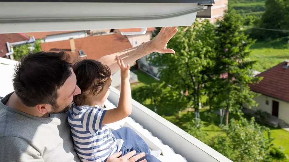 BMI Österreich Homeowners winken glücklich auf dem eigenen Balkon mit Sonnenschutz Bekannten und Freunden.