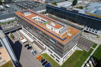 Drohnenbild der FUTUREbase in Wien-Floridsdorf auf das Gebäude und das Flachdach mit pv-Anlagen sowie Sicht auf die Parkplätze vor dem Gebäude
