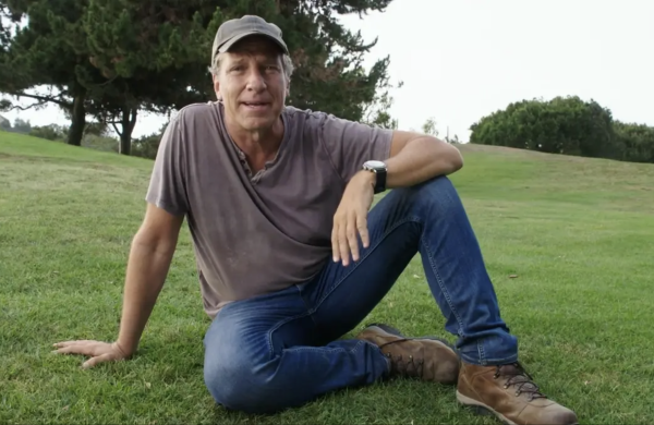 Mike Rowe, seated on a country meadow.