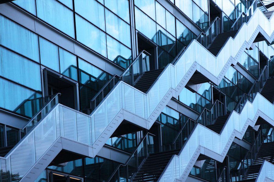 Façade moderne d'un bâtiment avec balcons en zigzag et panneaux de verre bleutés créant un motif géométrique distinctif.