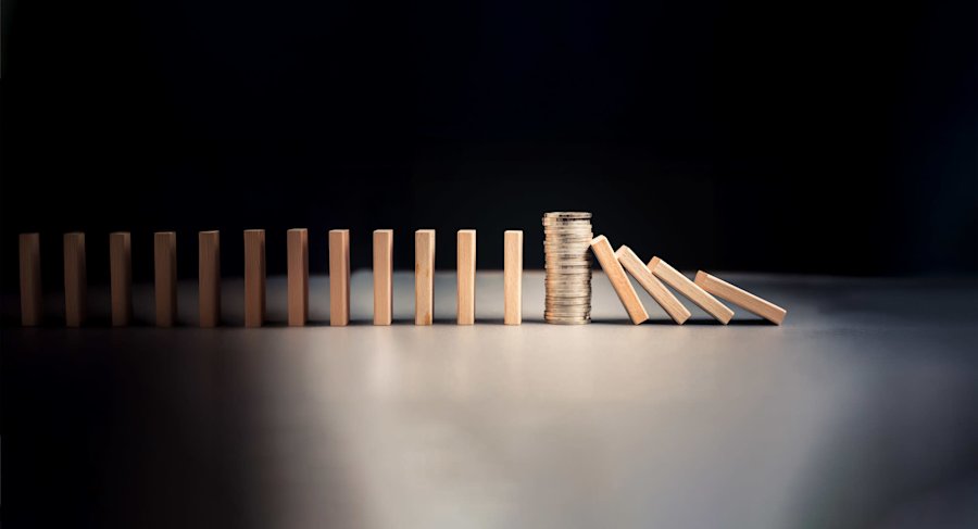 Houten dominostenen in een rij met een stapel munten die enkele omvallende dominostenen tegenhoudt tegen een donkere achtergrond.