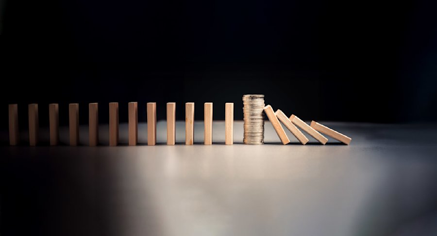Dominos en bois alignés avec une pile de pièces de monnaie au milieu, quelques dominos tombant à droite, sur fond noir.