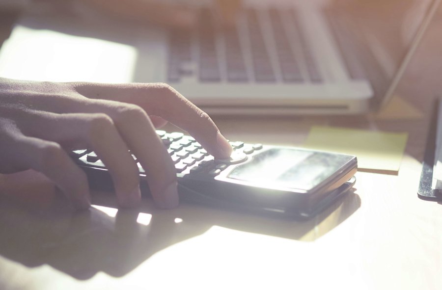 Main avec une calculatrice sur un bureau avec un ordinateur portable en arrière-plan