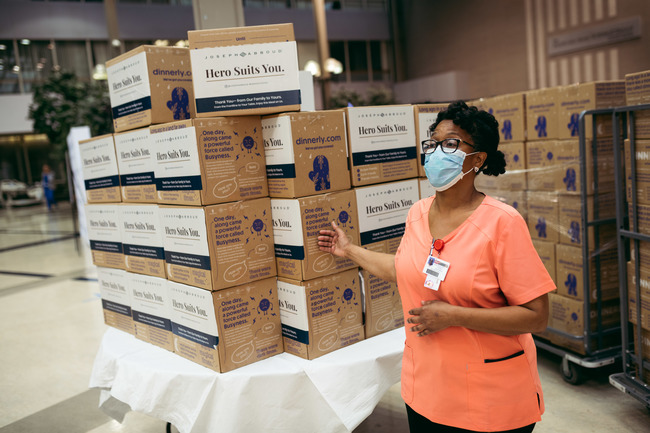 A hospital worker in mask and scrubs sets up piles of Dinnerly meal kits on a dolly. 