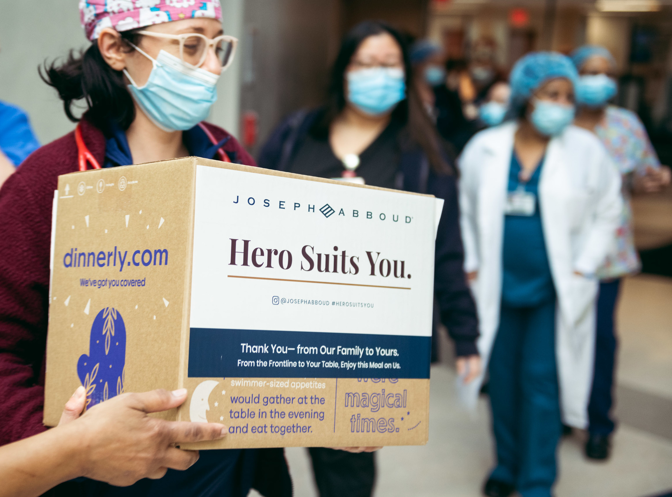 Hospital health care worker wearing mask and ppe receives food meal kit box as other nurses and doctors stand in line. 