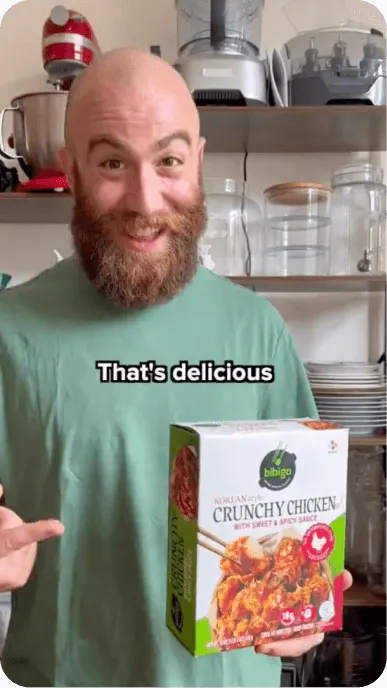 Bald creator with beard holds box of bibigo crunchy chicken dumplings. Text overlay says thats delicious.