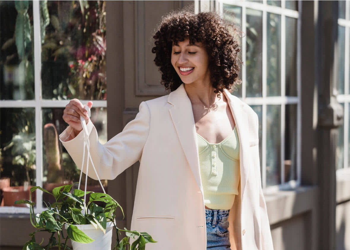 Woman with curly hair smiles while holding a hanging plant. Text overlay reads 100% easier with Later.