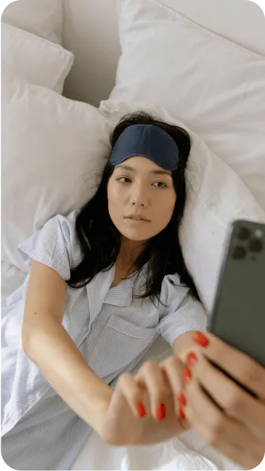 Woman with eye mask and pajamas takes a selfie lying in bed