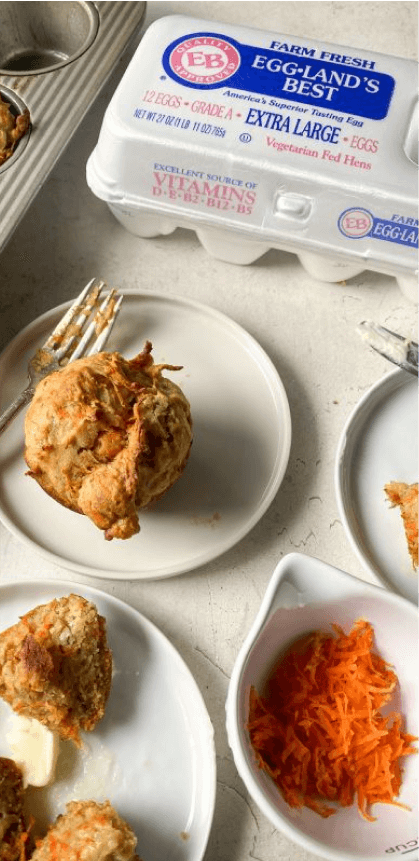 Plates of baked goods, a bowl of shredded carrots, and a carton of Eggland's Best eggs arranged on a kitchen counter