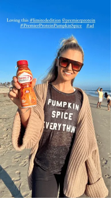 Creator poses on beach with pumpkin spice protein shake wearing a shirt that says pumpkin spice everything