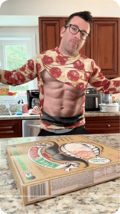 TikTok still of creator with glasses and pizza sweater posing next to pizza box on countertop