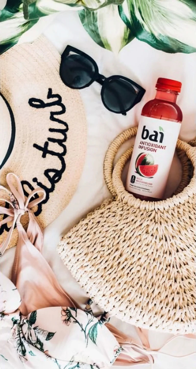 Close up of beach accessories - sunglasses, straw hat, purse and bathing suit and a bottle of Bai antioxidant infusion drink