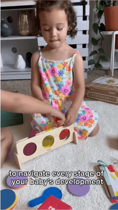 Small girl in floral dress plays with wooden toy from KiwiCo on living room floor