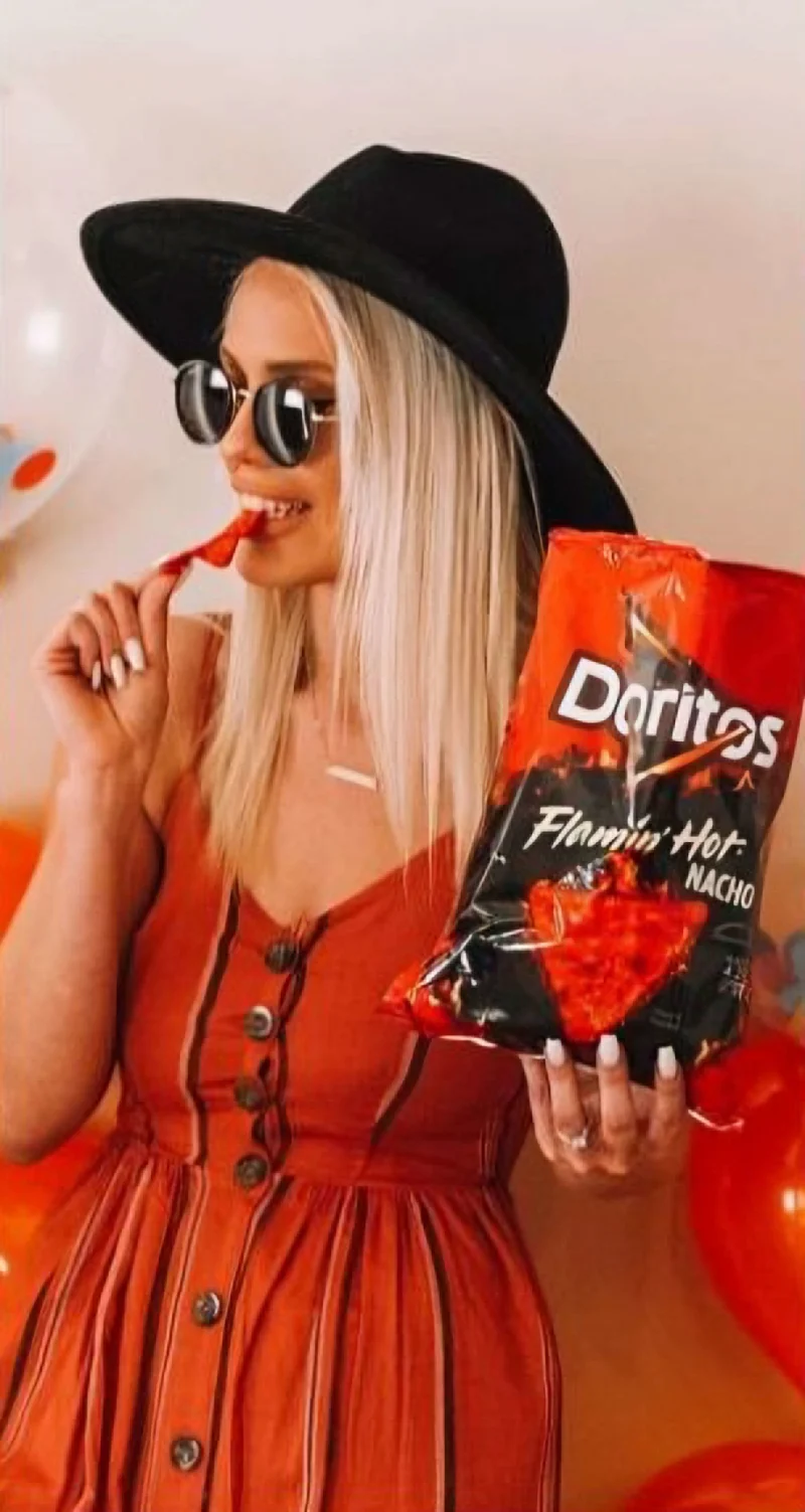Woman influencer in boho hipster outfit holding bag of Doritos Flamin Hot Nachos taking a bite of a Dorito