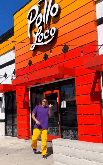An influencer in a purple shirt and yellow pants poses in front of an El Pollo Loco storefront