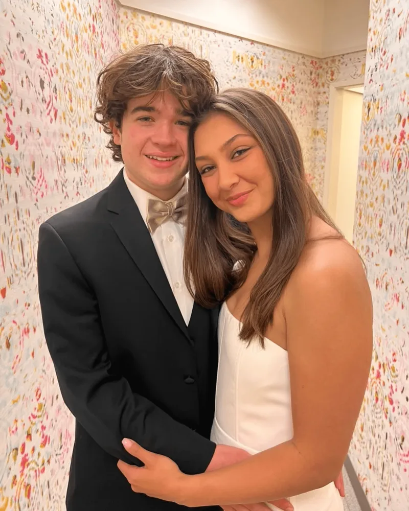 Creator in black tuxedo with bowtie poses with prom date in white dress