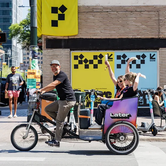 A Later-branded pedicab on a city street, its passenger waving.