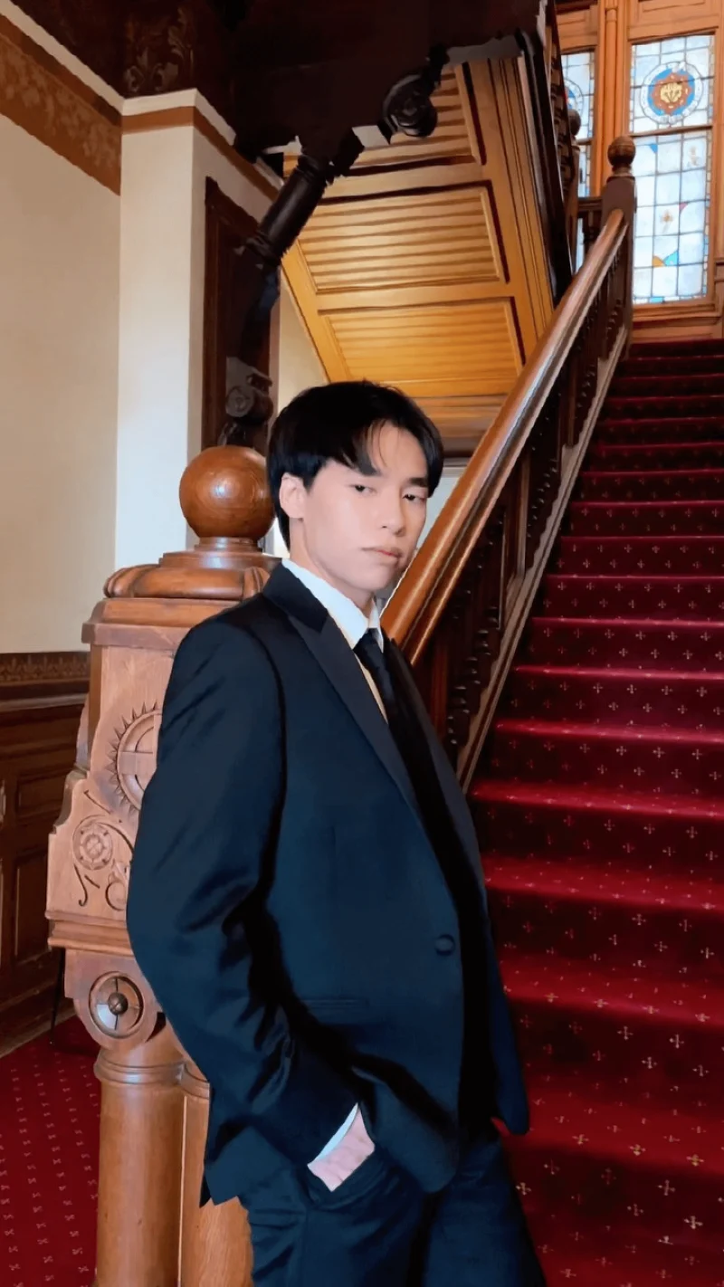Creator in black tuxedo poses in front of an indoor staircase with a red carpet