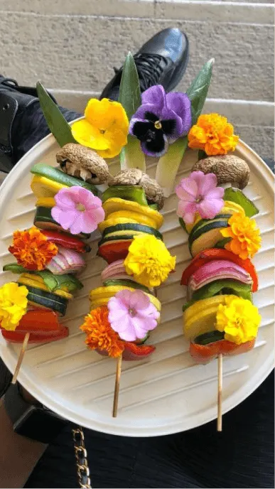 An aesthetic beige plate with three skewers of grilled vegetables with edible flowers
