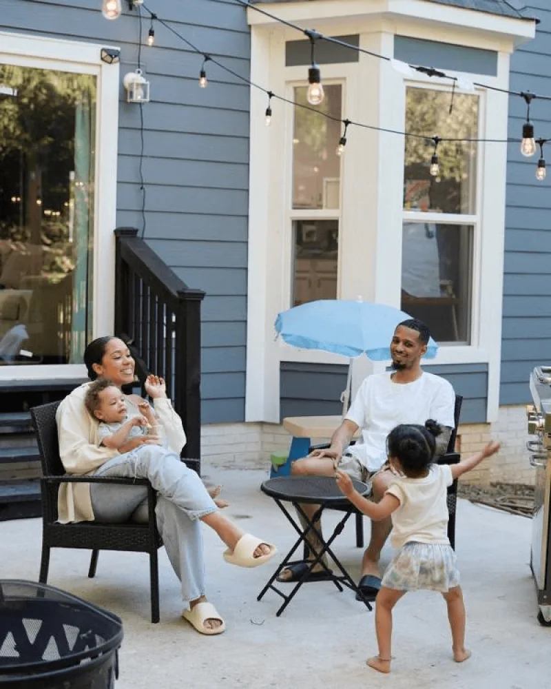 Parents with 2 children relaxing outside on the patio of a blue house with patio lights