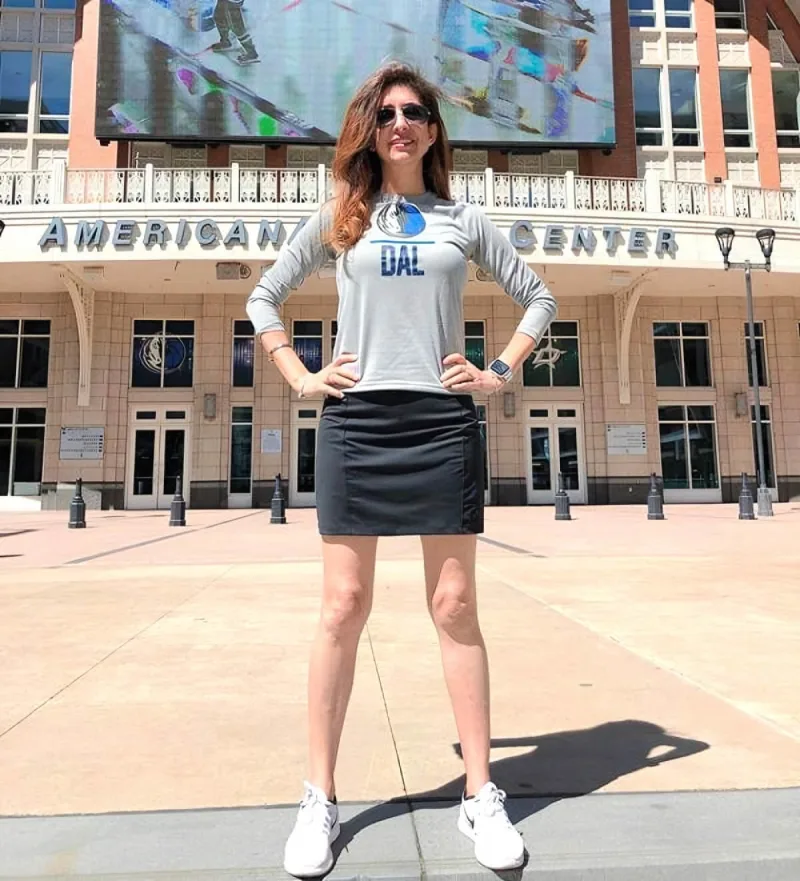 Woman in skirt and Mavericks shirt stands in front of a stadium