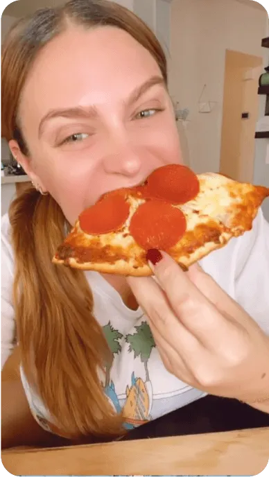 Instagram Reel still of a woman biting into a slice of pepperoni pizza