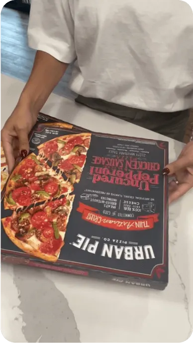 Creator holds box of Urban Pie pepperoni and chicken sausage pizza in TikTok still