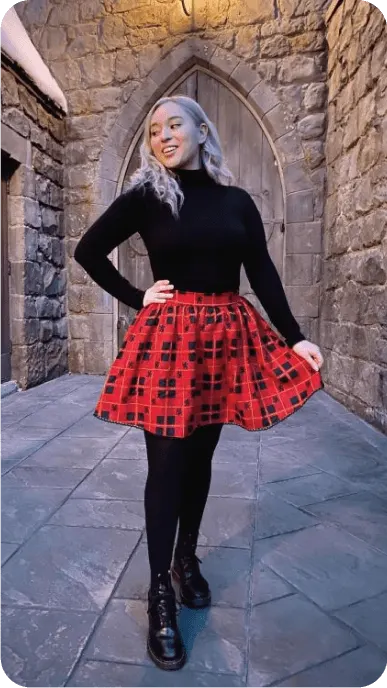 Creator poses outside stone wall with door wearing a red skirt from Hot Topic
